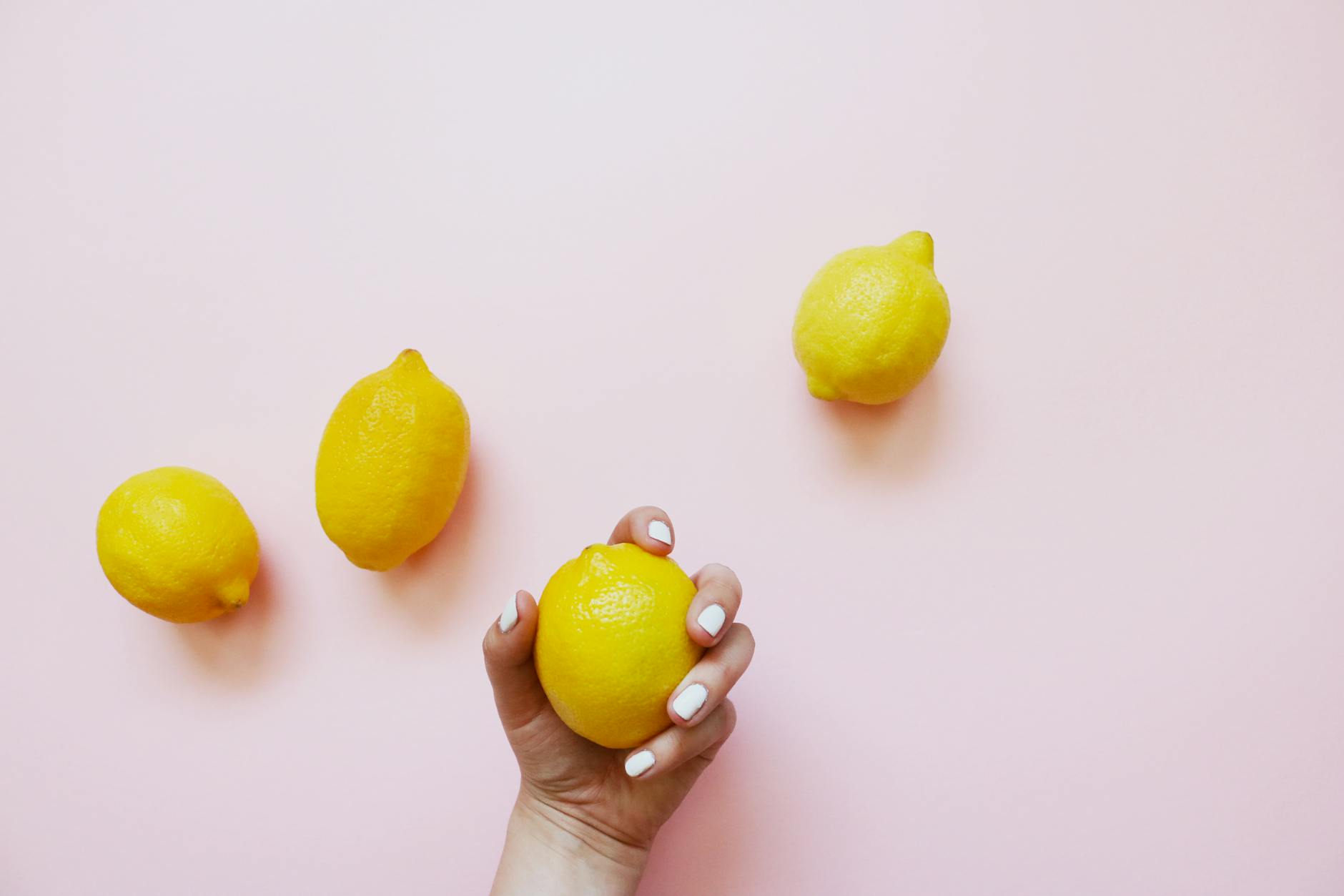 A hand holding fresh lemons on a soft pink background, representing fresh starts with pleasure and sensitivity.