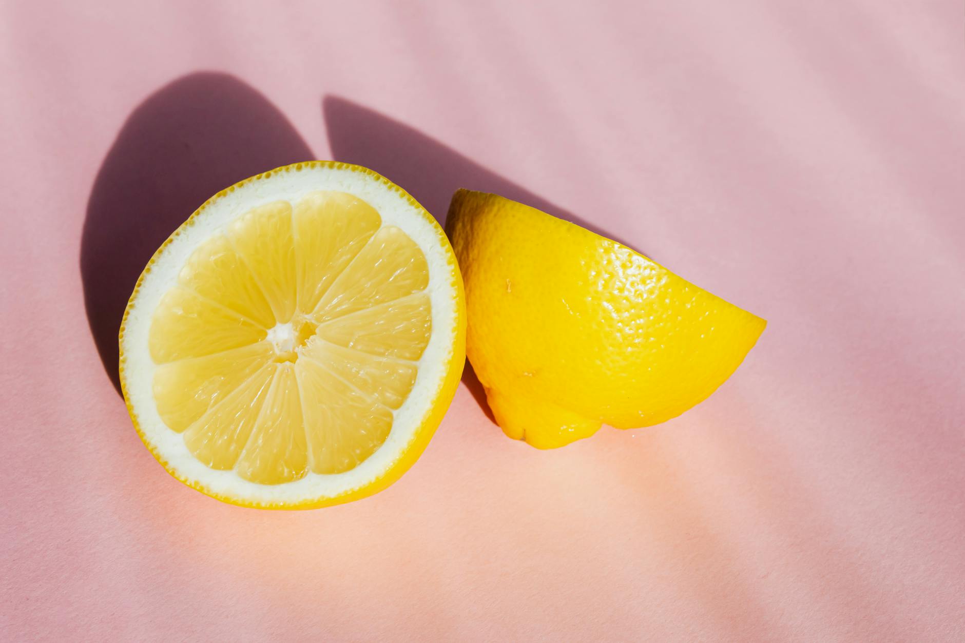 Fresh lemon halves on a pink background in sunlight, representing freshness and the lemon vibrator theme