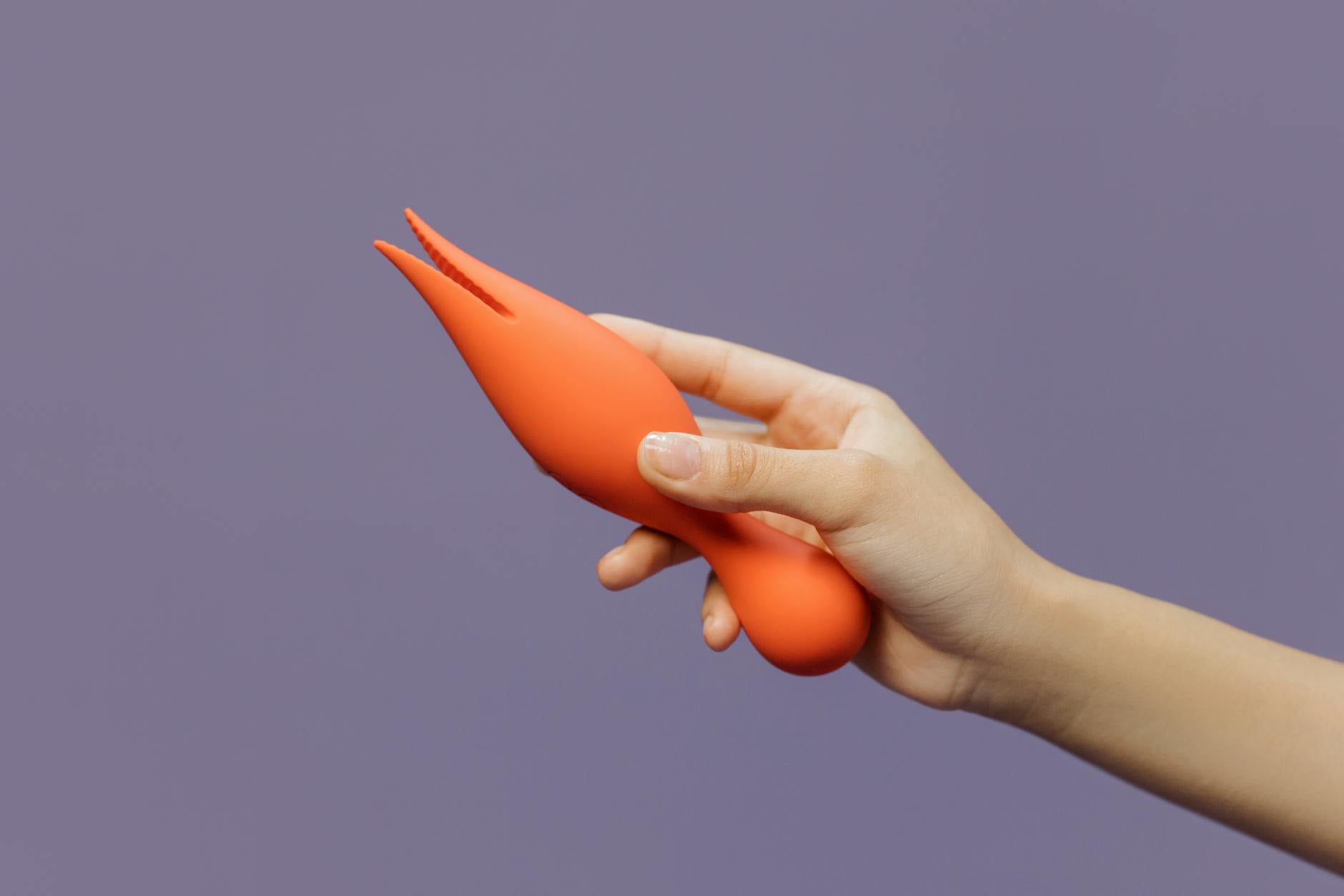 A hand holding a yellow lemon vibrator against a minimalist purple backdrop, representing modern sexual wellness.