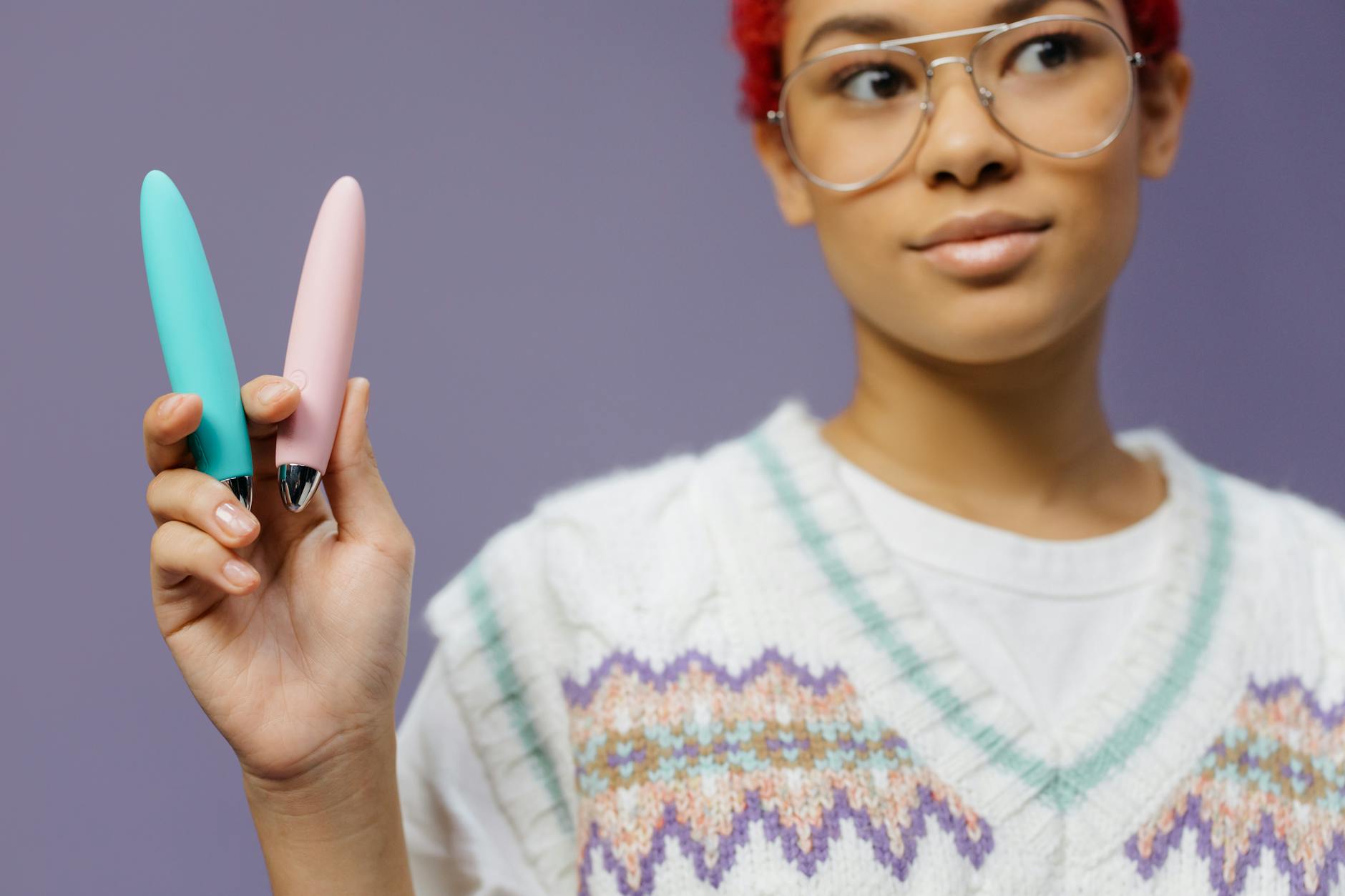 Woman holding colorful vibrators against purple background, showing confidence and openness